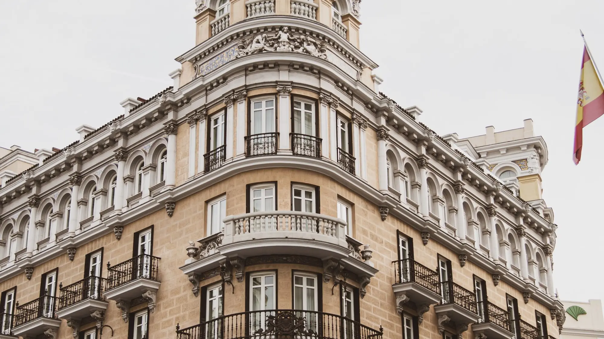 Esquina de un edificio clásico de piedra en el centro de Madrid, con balcones de forja y una bandera de España