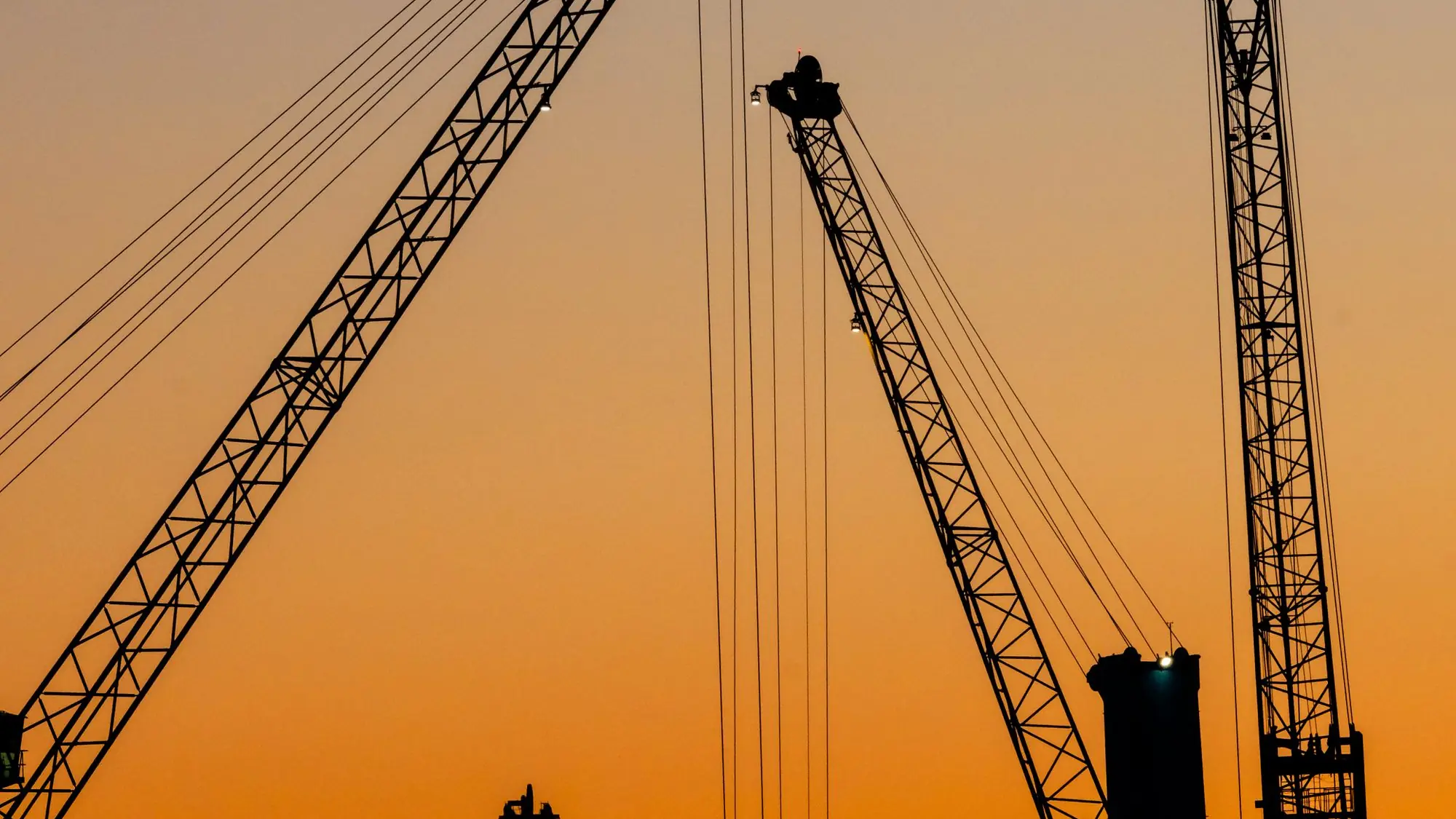 Grúas torre recortadas en negro contra el cielo naranja del atardecer