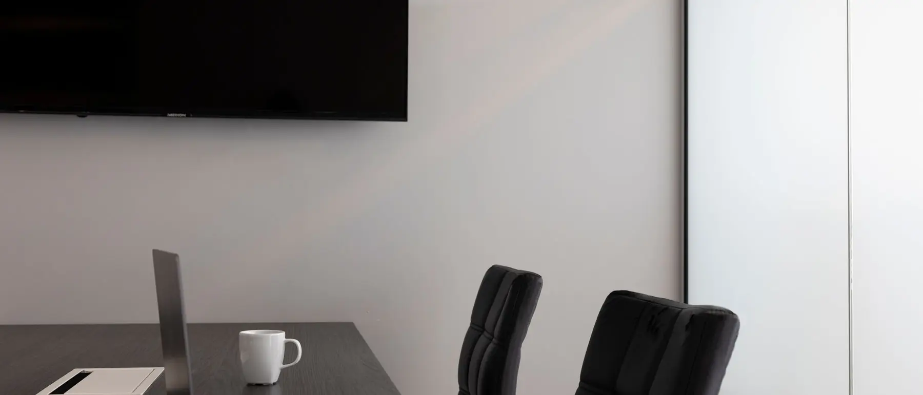 Sala de reuniones vacía con un portátil y una taza sobre la mesa oscura